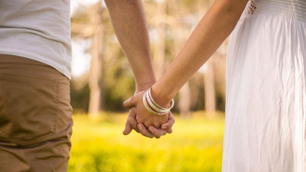 foto de casal com close nas mãos dadas em local com árvores e grama.