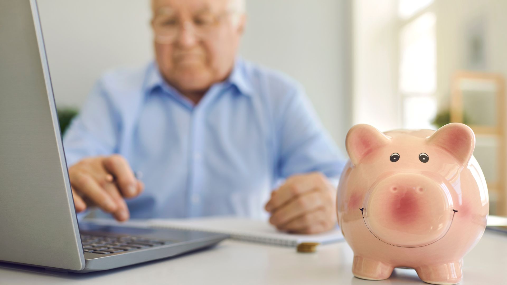Idoso usando computador com um porco cofrinho