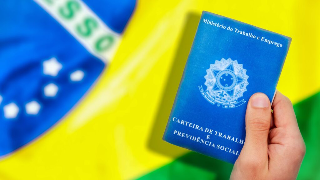 Mão segurando Carteira de Trabalho sobre a bandeira do Brasil