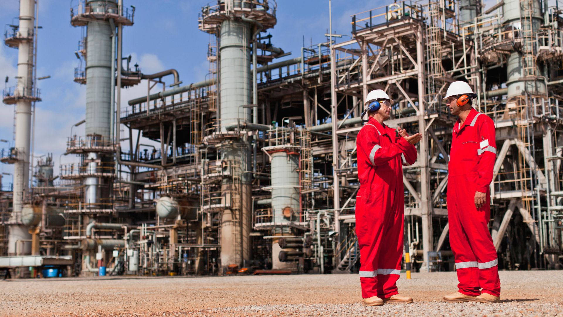 Dois homens de macacão e EPIs em uma refinaria