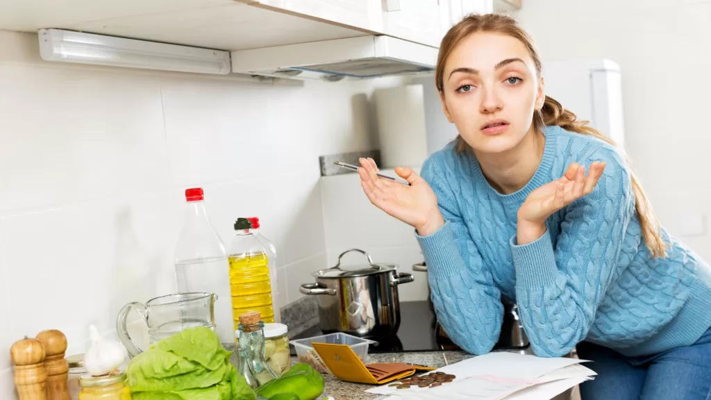 Jovem mulher fazendo as contas na cozinha e sem saber o que fazer